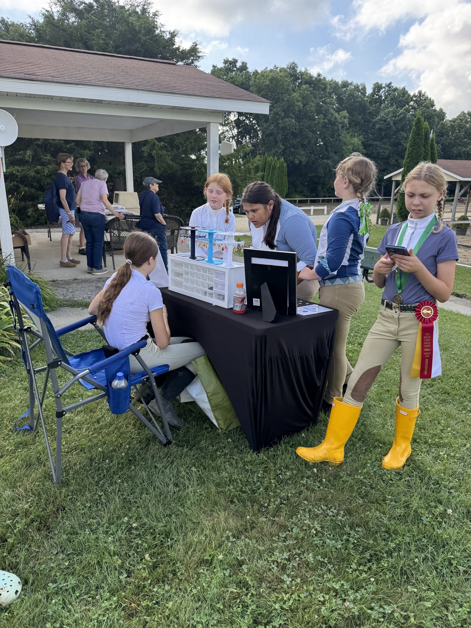 Junior riders in show breeches and tall boots at the booth, championship ribbons in hand