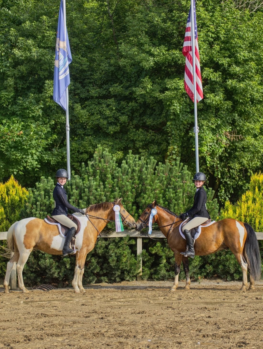 Sadie and Olivia mounted, ribbons in hand, in front of state and U.S. flags